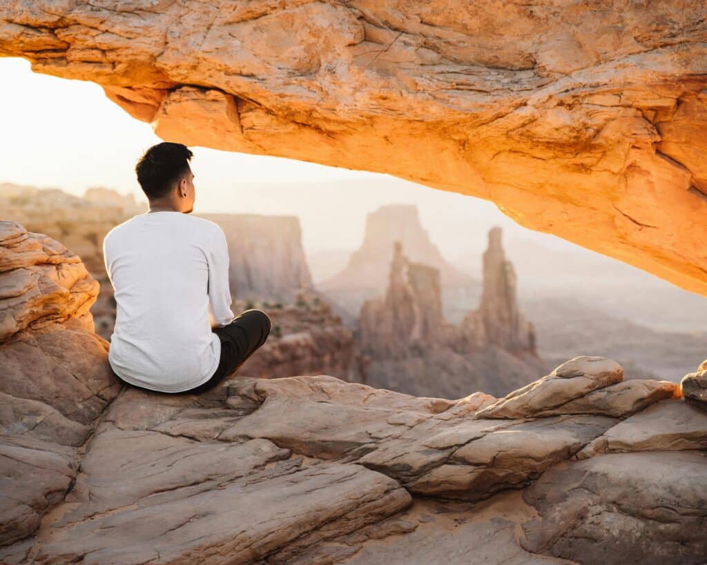 pexels-alexazabache-5117916 - Vintage at Tabernacle Man sitting on a rocky ledge in a desert canyon, with sandstone formations and distant arches in warm evening light